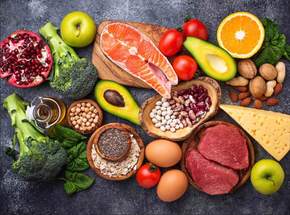 A colorful spread of whole foods including salmon, vegetables, fruit, legumes, nuts, eggs, and grains
