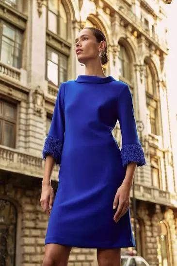 Woman in a royal blue shift dress with fringed cuffs on a city street