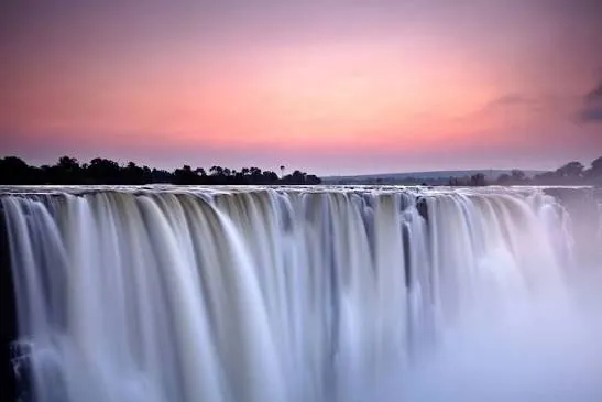 Wide curtain of Victoria Falls beneath a pink and purple dusk sky