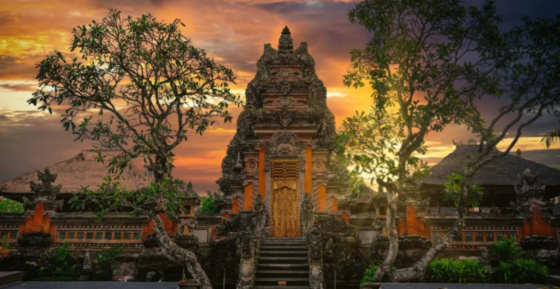 Balinese temple gate at sunset with dramatic orange and gold clouds and trees framing it