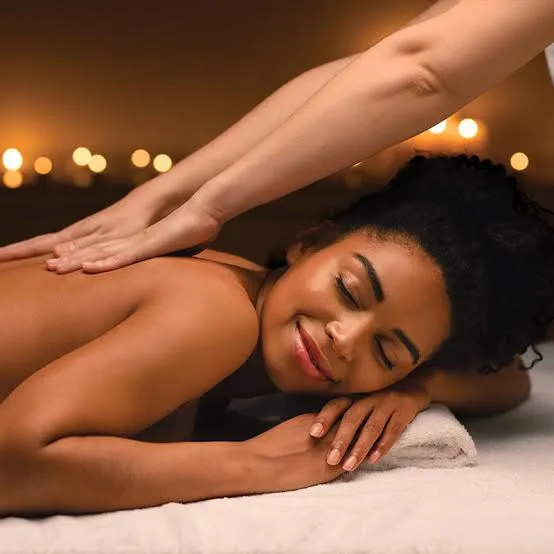 A woman smiling peacefully with closed eyes while receiving a warm, candle-lit massage at a spa