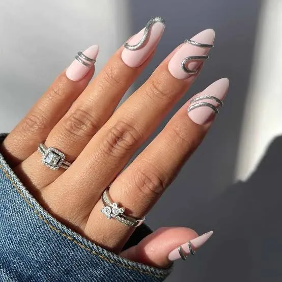 Pink almond nails with sculpted silver wave details, styled with silver rings and denim