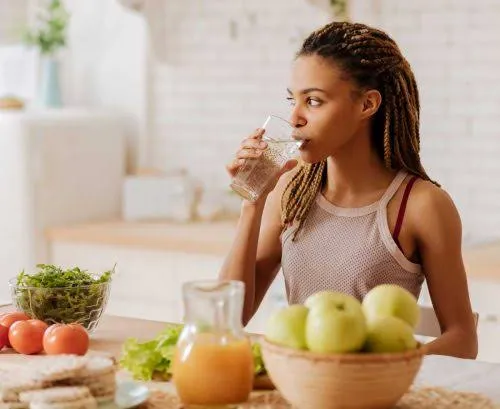 A woman drinking a glass of water while sitting at a table