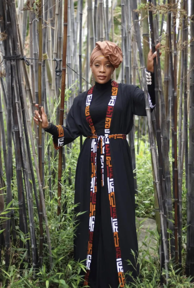 Kaleema Overton Ameen standing among bamboo in a black robe with patterned trim